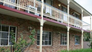 A two-story building with a brick facade, multiple windows, and a balcony with white railings.