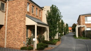 A residential street with brick houses, a paved driveway, and a clear sky. - Grand Manor Motor Inn - Queanbeyan (Queanbeyan East)