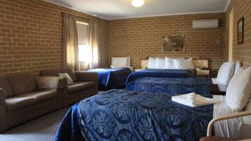 A hotel room with two beds, a sofa, and a brick wall.