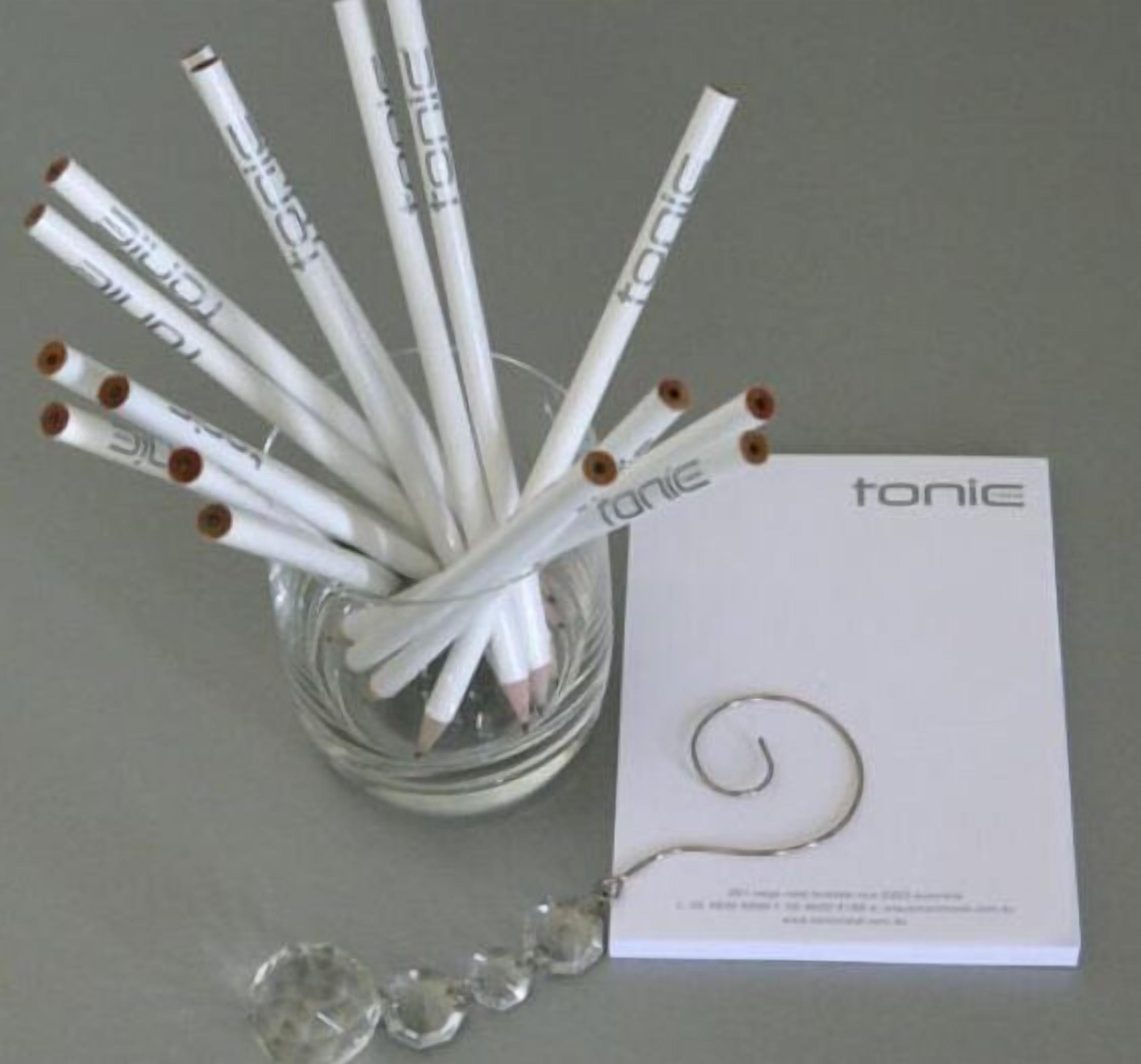 A glass container holding white pencils with brown erasers and a white card with the word "tonic" on it.