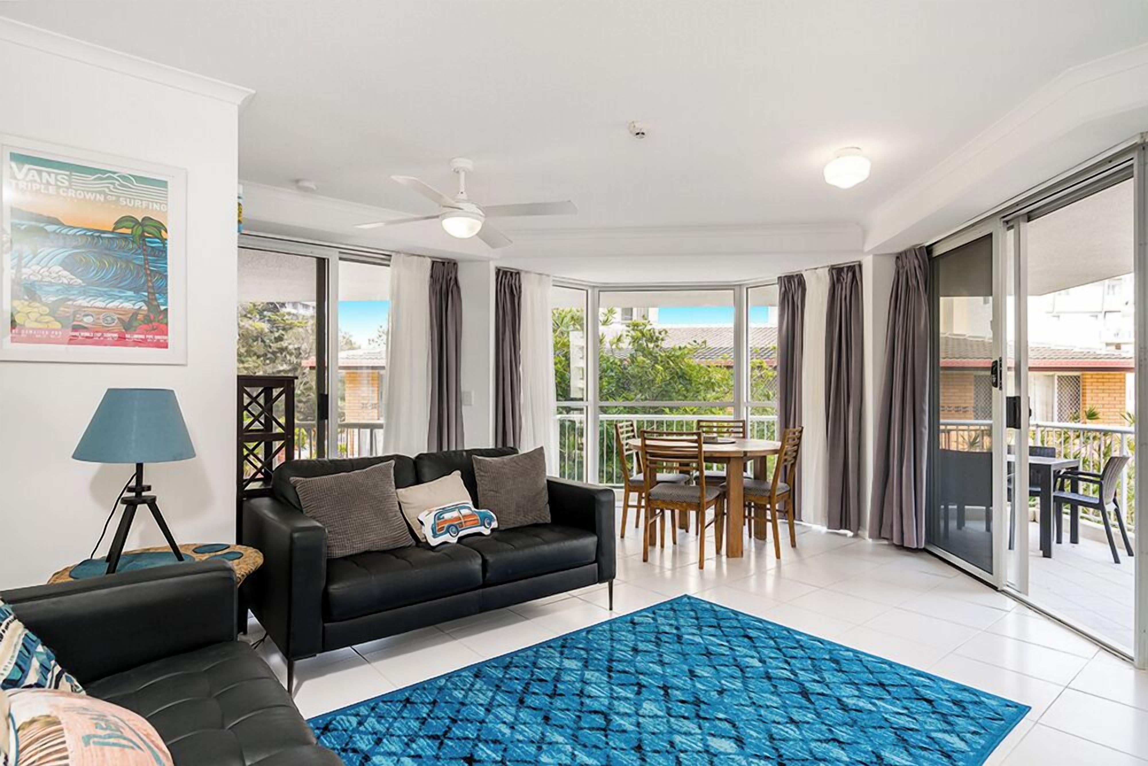 Uma sala de estar moderna com um sofá preto, um tapete padronado azul e uma área de jantar com mesa e cadeiras.