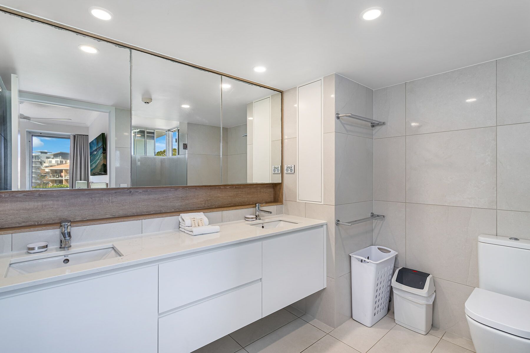 A modern bathroom with a large mirror, a sink, a shower, and a toilet.
