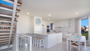 A modern kitchen with white cabinets, a central island with stools, and a large clock on the wall. - Rainbow Bay Resort (Coolangatta)