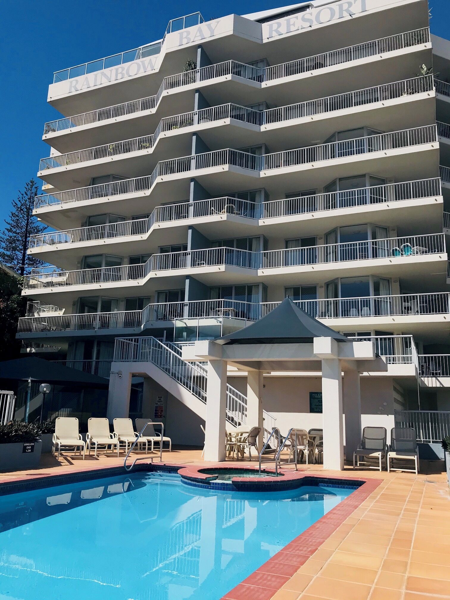 Un hôtel à plusieurs étages doté de balcons, d’une piscine et de chaises longues.