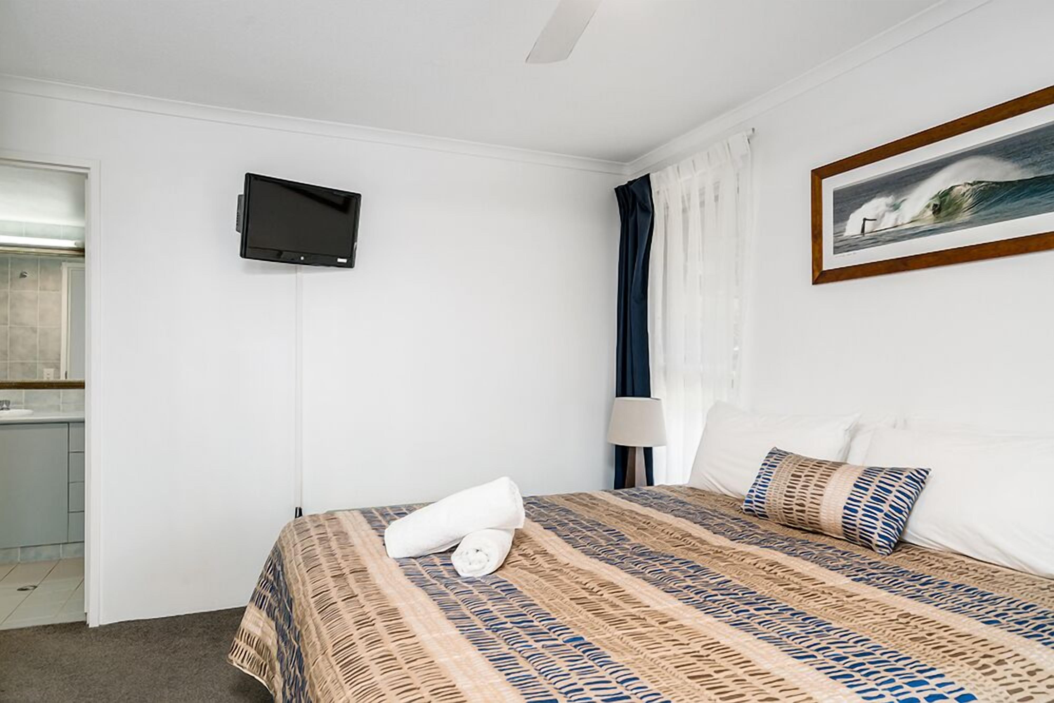Een hotelkamer met een bed, een televisie, een schilderij en een badkamer, zichtbaar door een geopende deur.