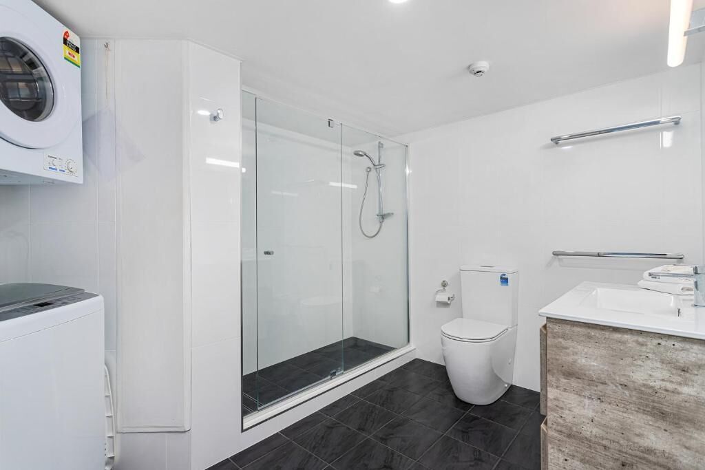 A modern bathroom with a glass-enclosed shower, a white toilet, and a washing machine.