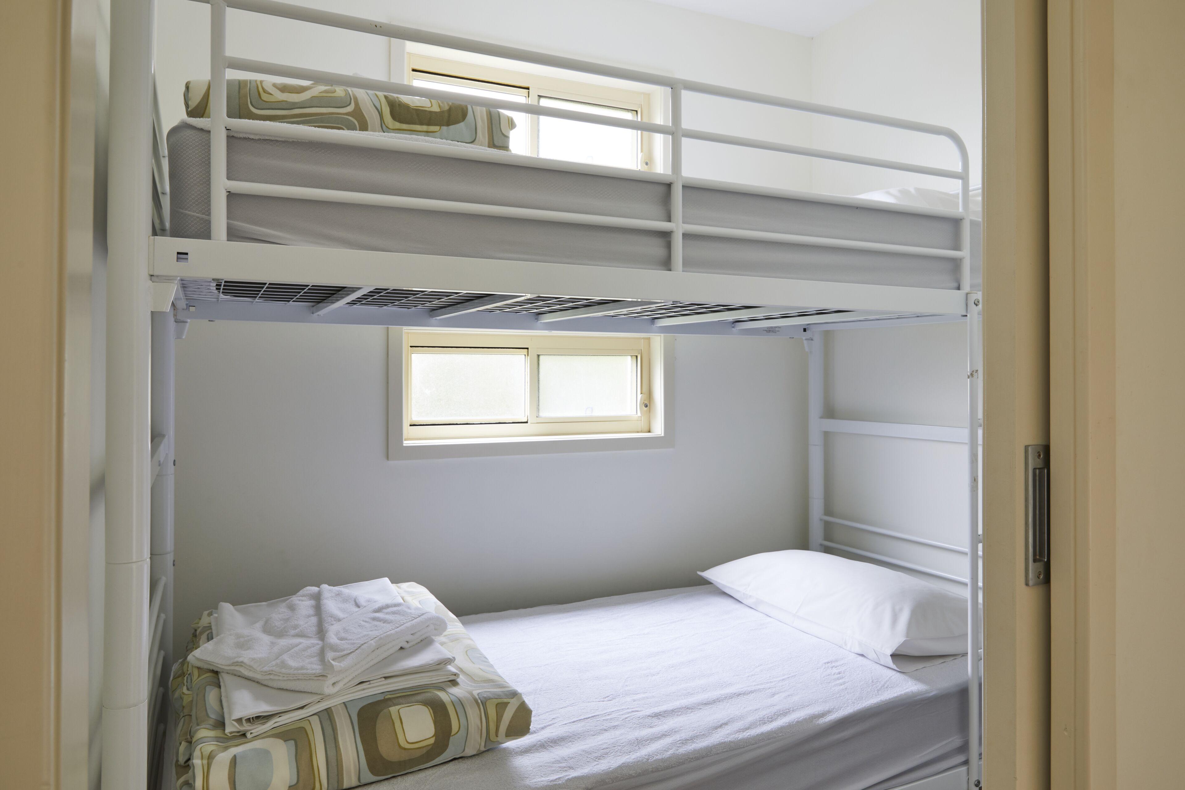 A bunk bed room with a window, a single bed, and a pile of folded towels.