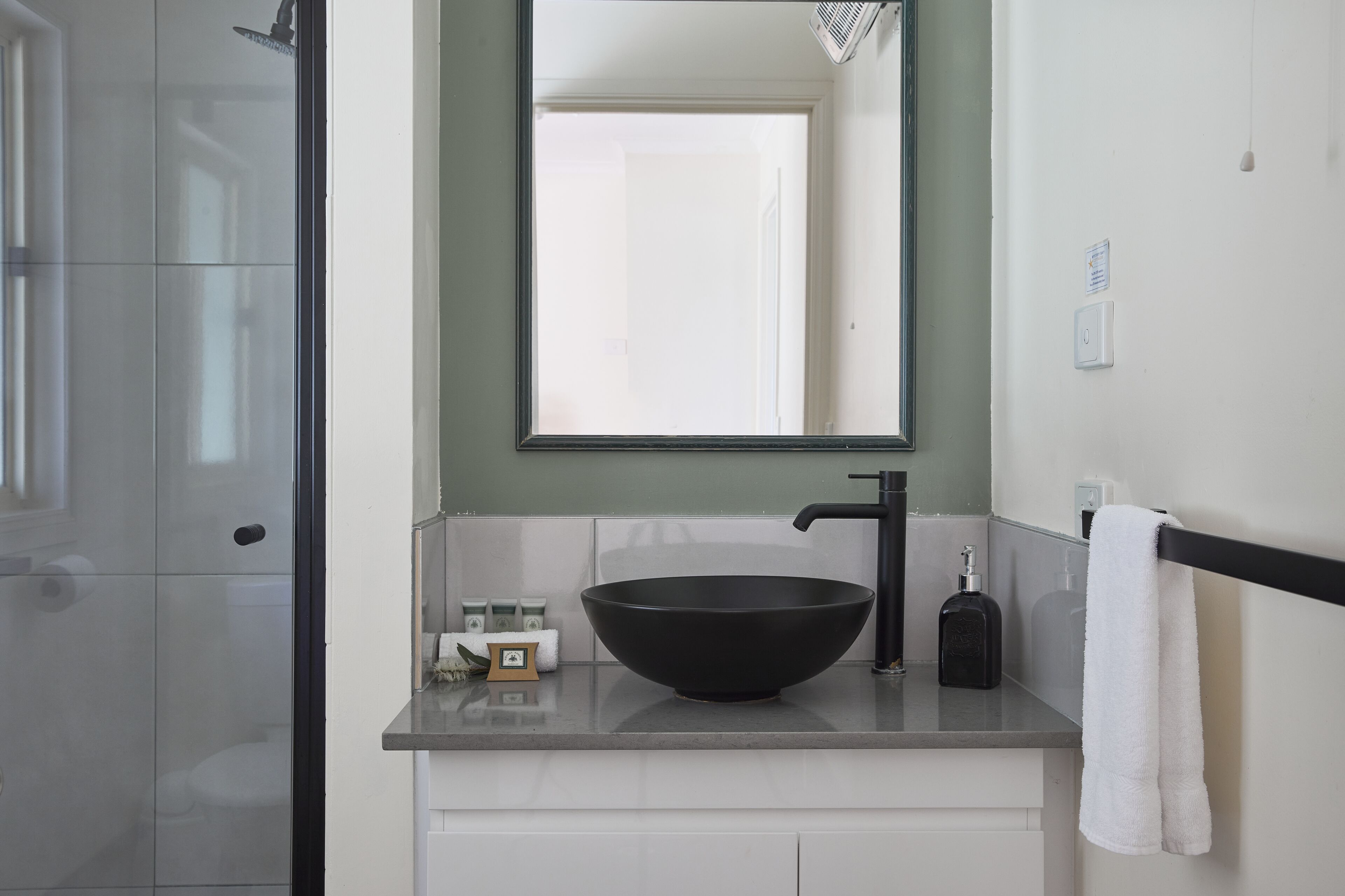 Une salle de bain moderne avec un lavabo sur colonne noir, un miroir et un porte-serviettes.