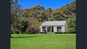 A single-story house with a porch, surrounded by a well-maintained lawn and dense trees. - Mystery Bay Cottages (Mystery Bay)