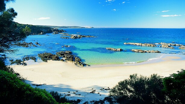 A beach with clear blue water, rocky outcrops, and a sandy shore. - Mystery Bay Cottages (Mystery Bay)