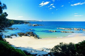 Una playa con aguas azules cristalinas, afloramientos rocosos y una orilla arenosa.