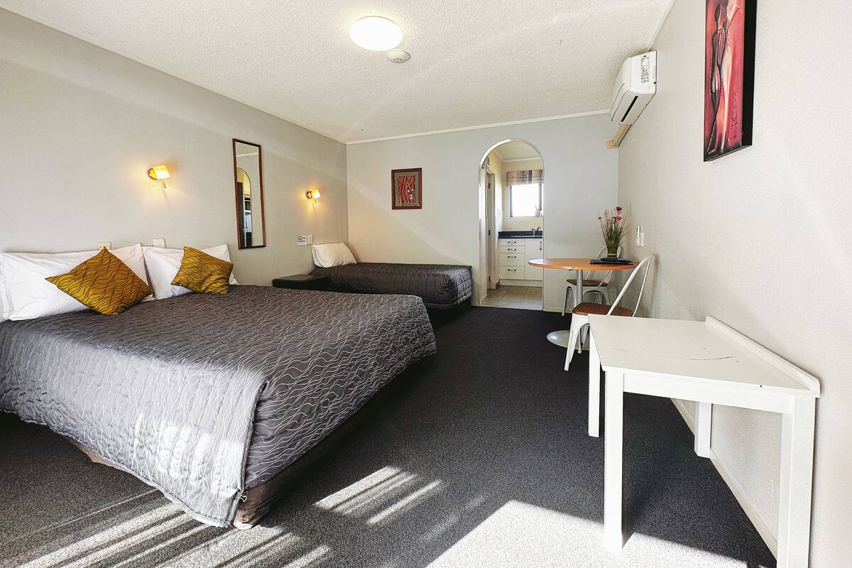 A hotel room with two beds, a desk, a chair, and a kitchenette.