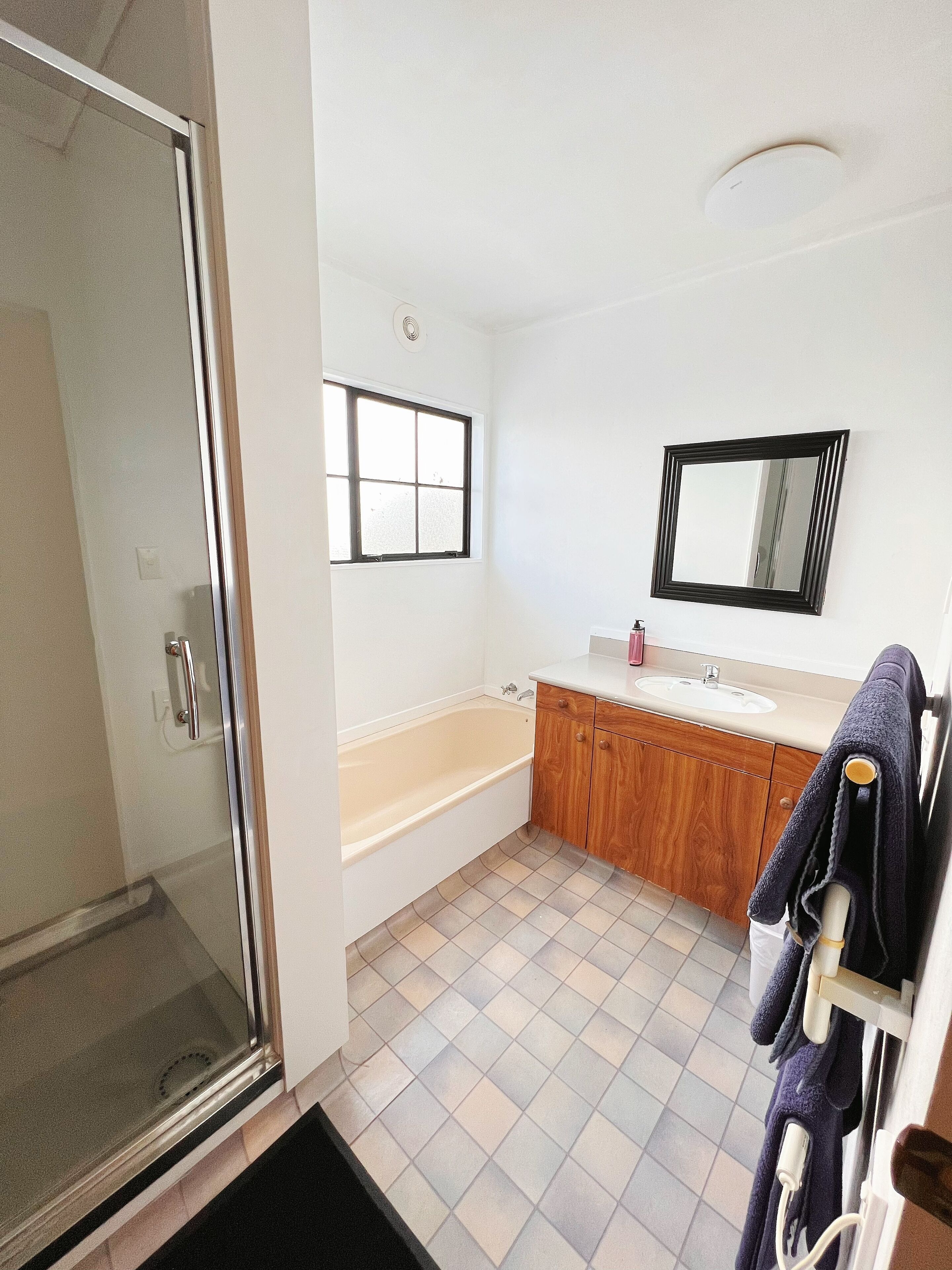 Un baño con cabina de ducha de vidrio, bañera, tocador de madera con lavabo y espejo en la pared.