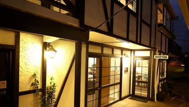 A reception area with a glass door, a sign indicating 'RECEPTION', and a small outdoor seating area with tables and chairs. - Kingswood Manor Motel (Whangarei)