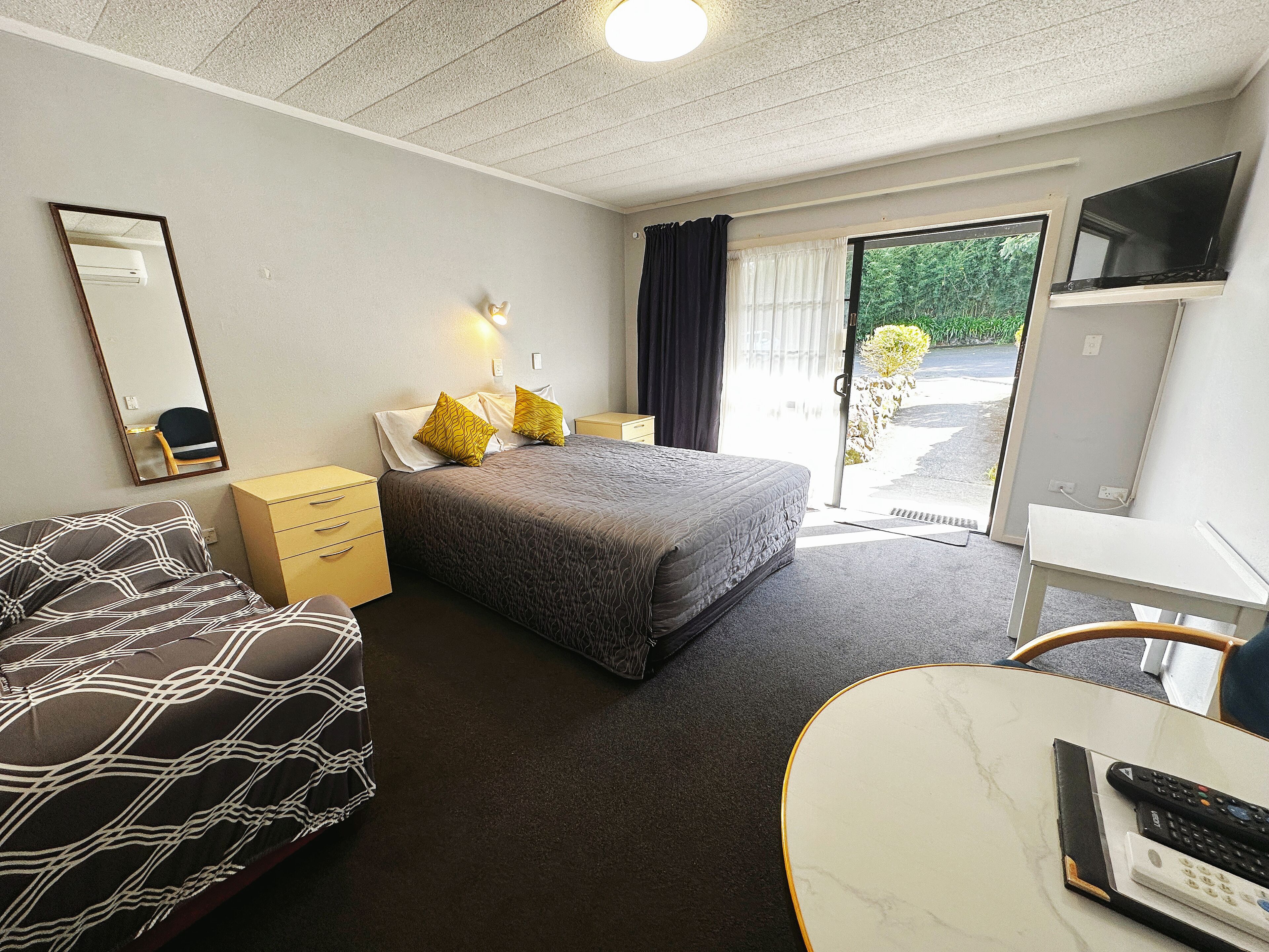Hotellihuone, jossa on sänky, sohva, työpöytä, televisio ja ikkuna, josta on näkymä vehreään maisemaan.