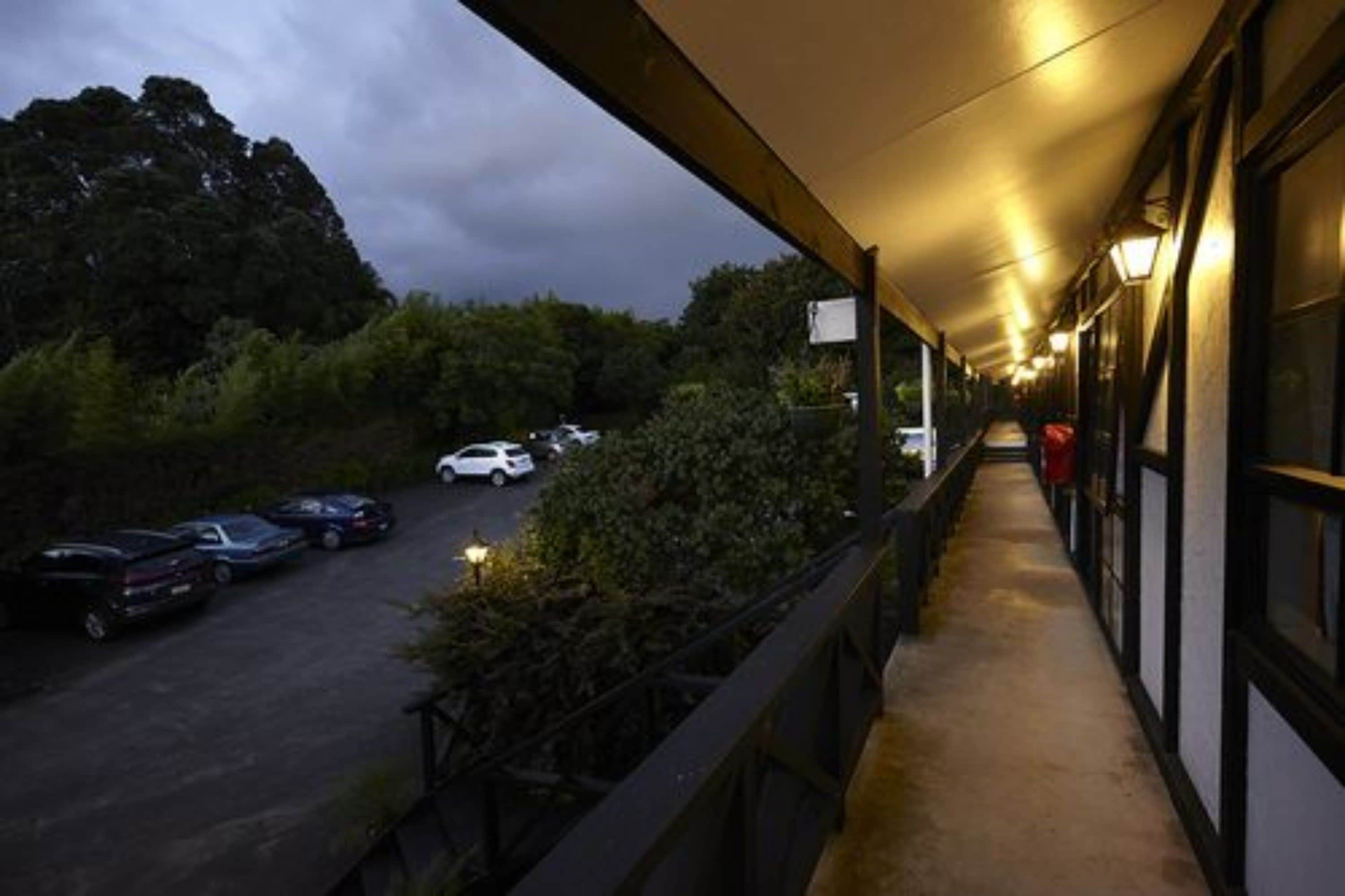 A covered outdoor corridor with a view of parked cars and trees.
