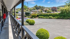 A covered outdoor area with a concrete floor, a railing, and a view of a parking lot and greenery. - Kingswood Manor Motel (Whangarei)