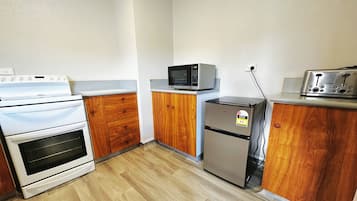 A kitchen with wooden cabinets, a stainless steel refrigerator, a microwave, a stove, and a toaster.