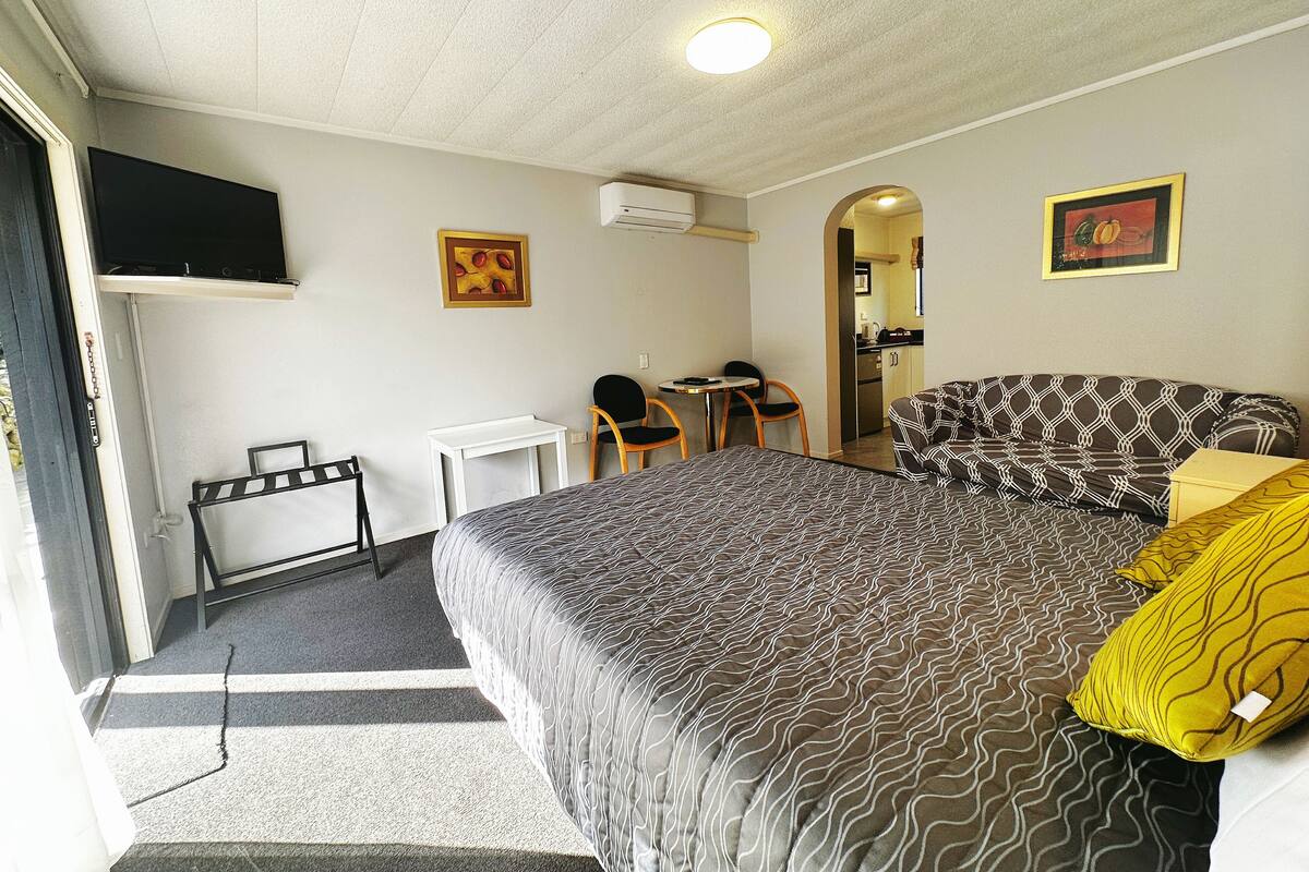 A hotel room with a bed, a desk, a chair, a television, and a kitchenette.