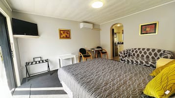 A hotel room with a bed, a desk, a chair, a television, and a kitchenette.