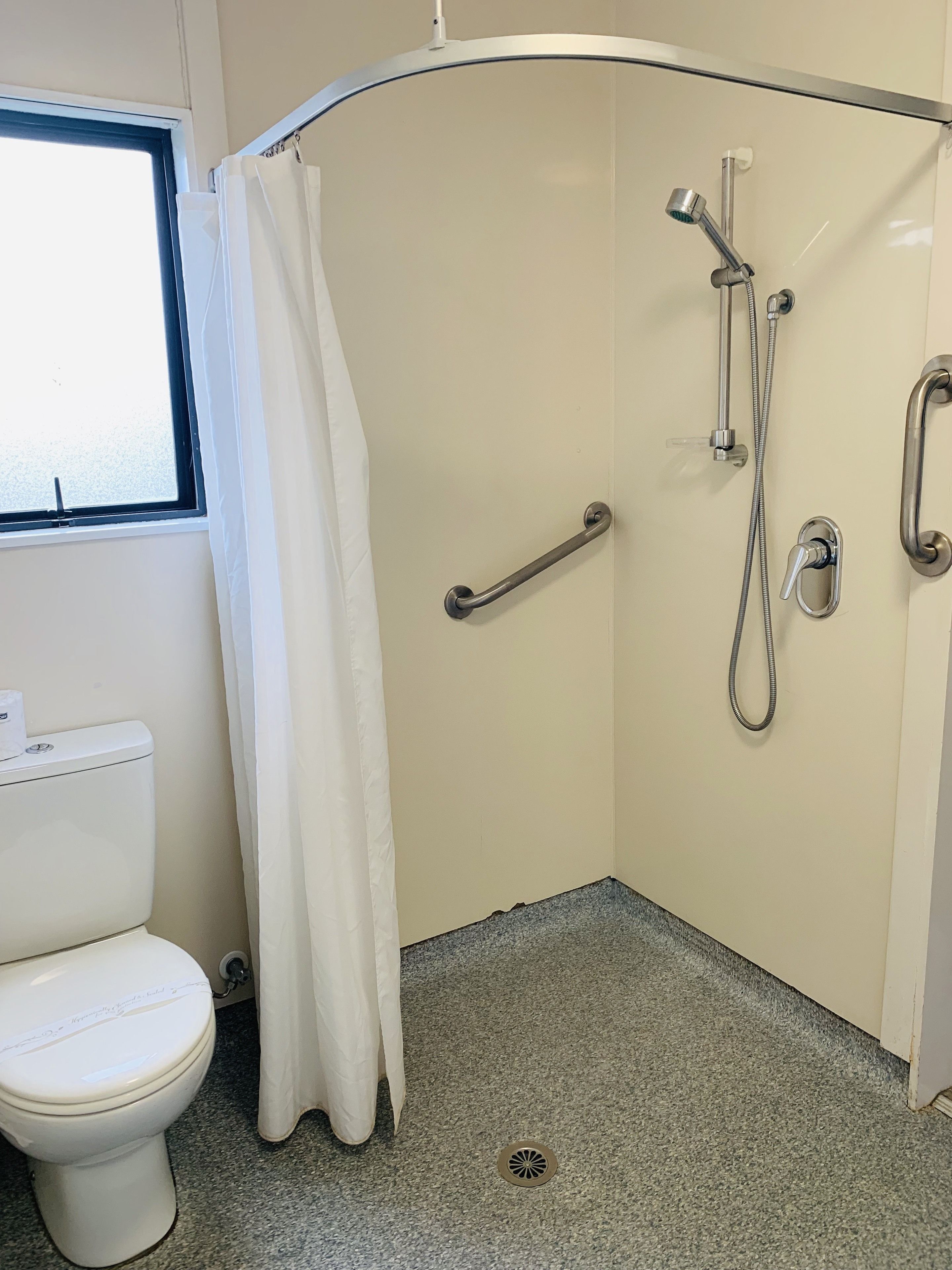 Une salle de bain avec une douche, des toilettes et une fenêtre.