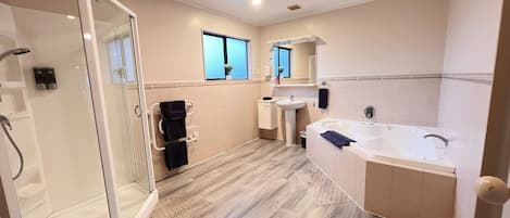 Un baño moderno con cabina de ducha de vidrio, ducha a ras de suelo, bañera grande y lavamanos sobre pedestal.