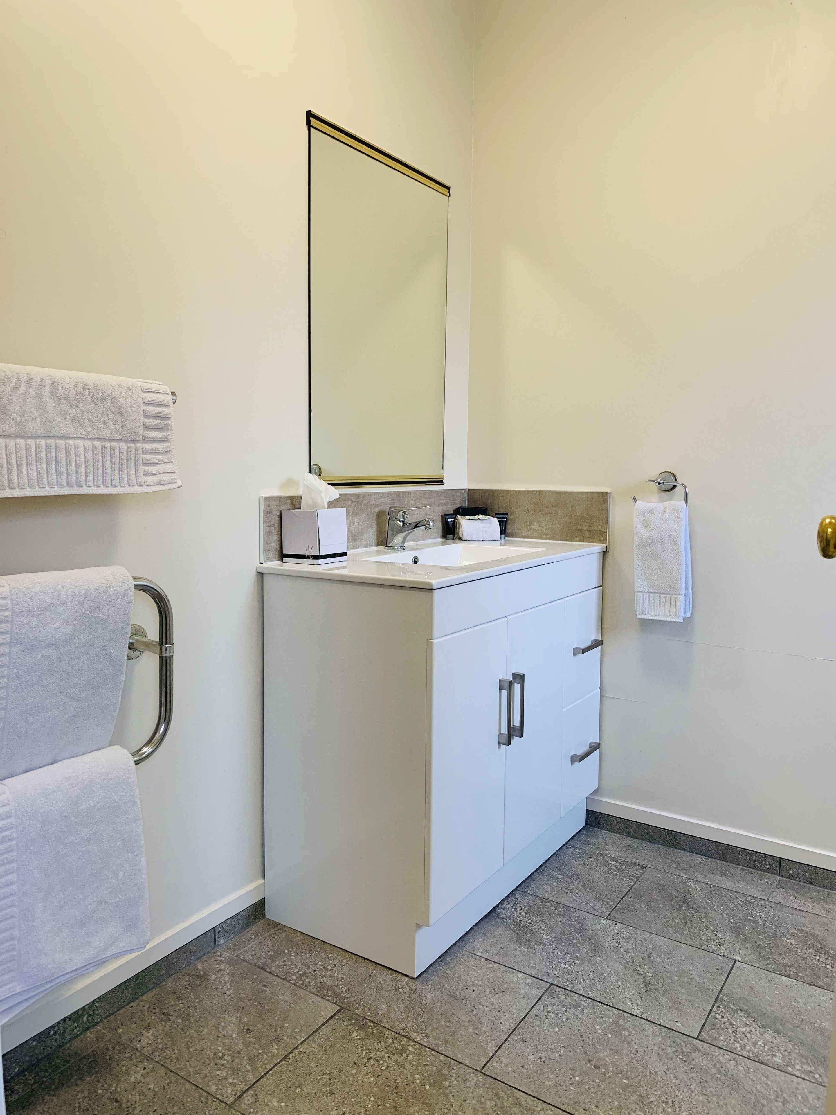 A bathroom with a white vanity, a mirror, a towel rack, and a toilet paper holder.