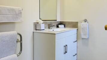 A bathroom with a white vanity, a mirror, a towel rack, and a toilet paper holder.