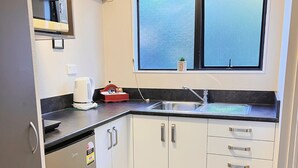 A compact kitchen with a built-in refrigerator, a sink, and a window with a view. - Kingswood Manor Motel (Whangarei)