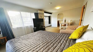A hotel room with a large bed, a desk, a chair, and a TV. - Kingswood Manor Motel (Whangarei)