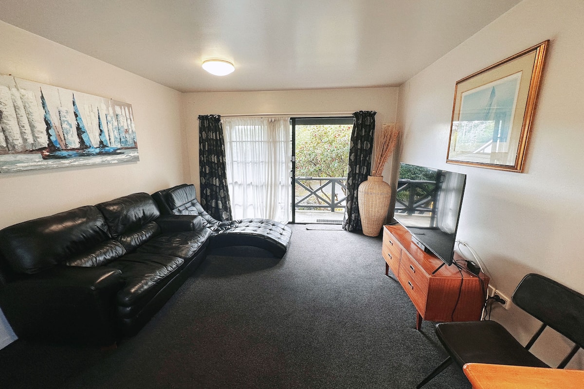 A living room with a black leather sofa, a wooden cabinet, a television, and a painting on the wall.