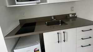 A compact kitchen with white cabinets, a built-in microwave, a sink, and a small refrigerator. - AAA Northlands Motel (Christchurch)