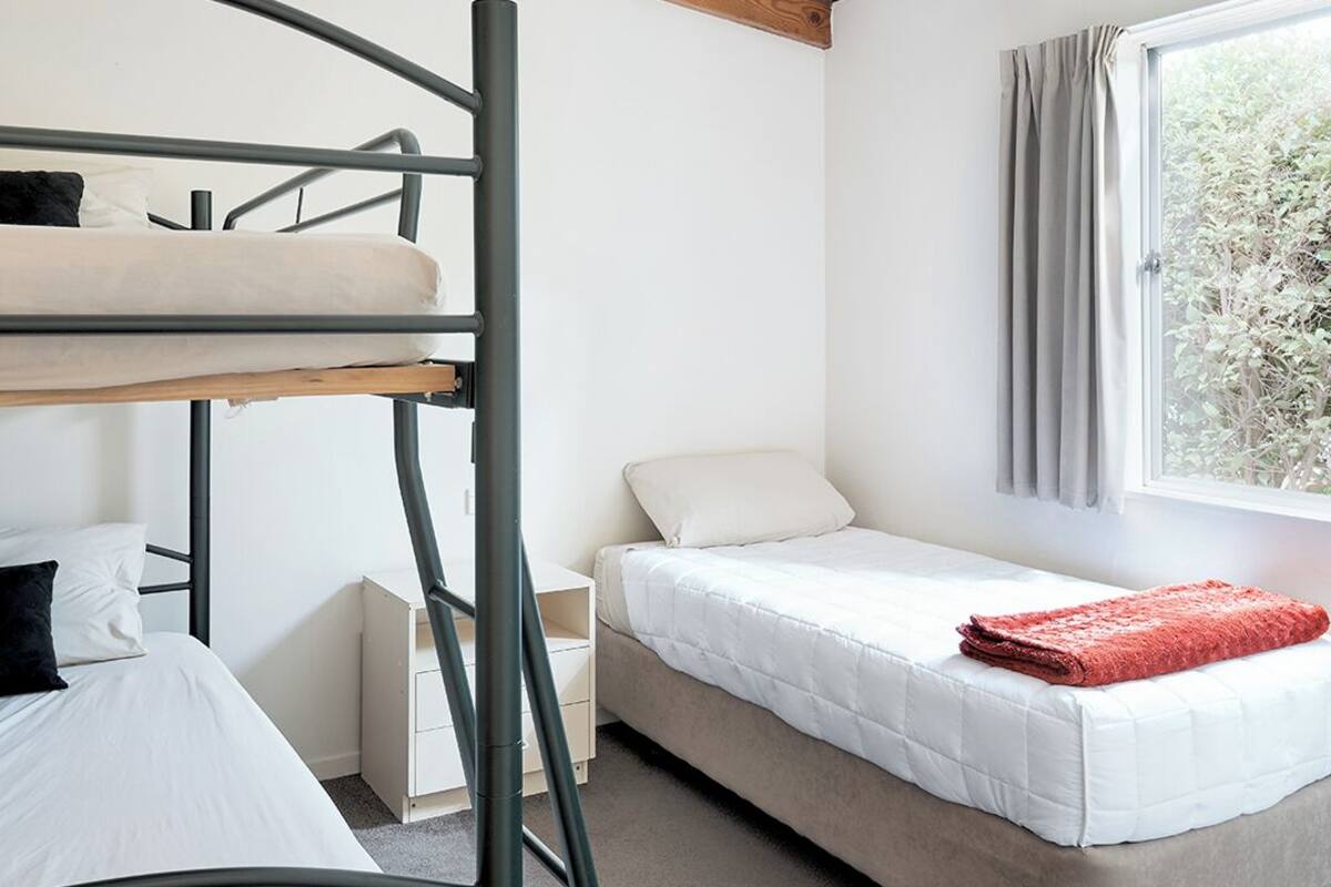 Une chambre avec des lits superposés, un lit simple, une fenêtre avec des rideaux et un luminaire au plafond.