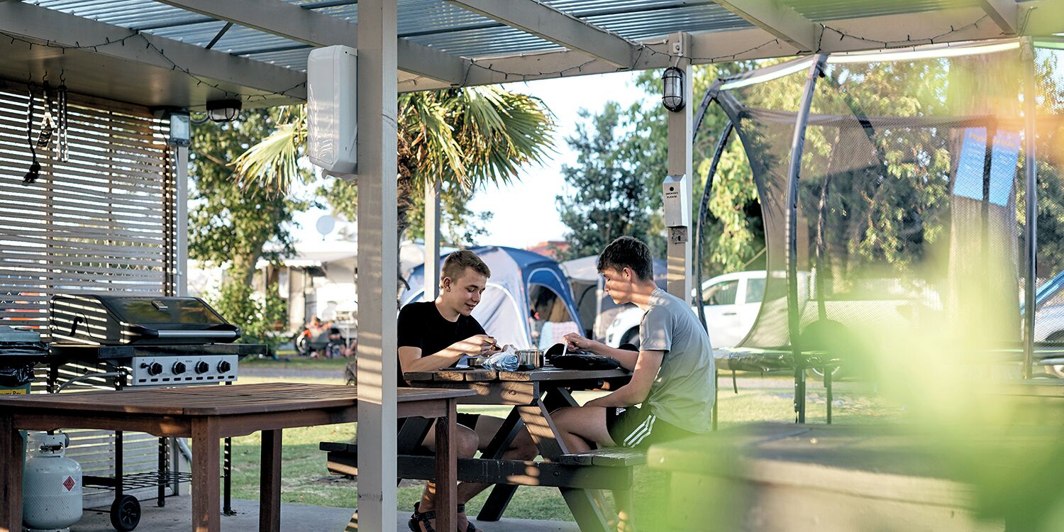 A covered outdoor area with a grill, picnic table, and a tent in the background.