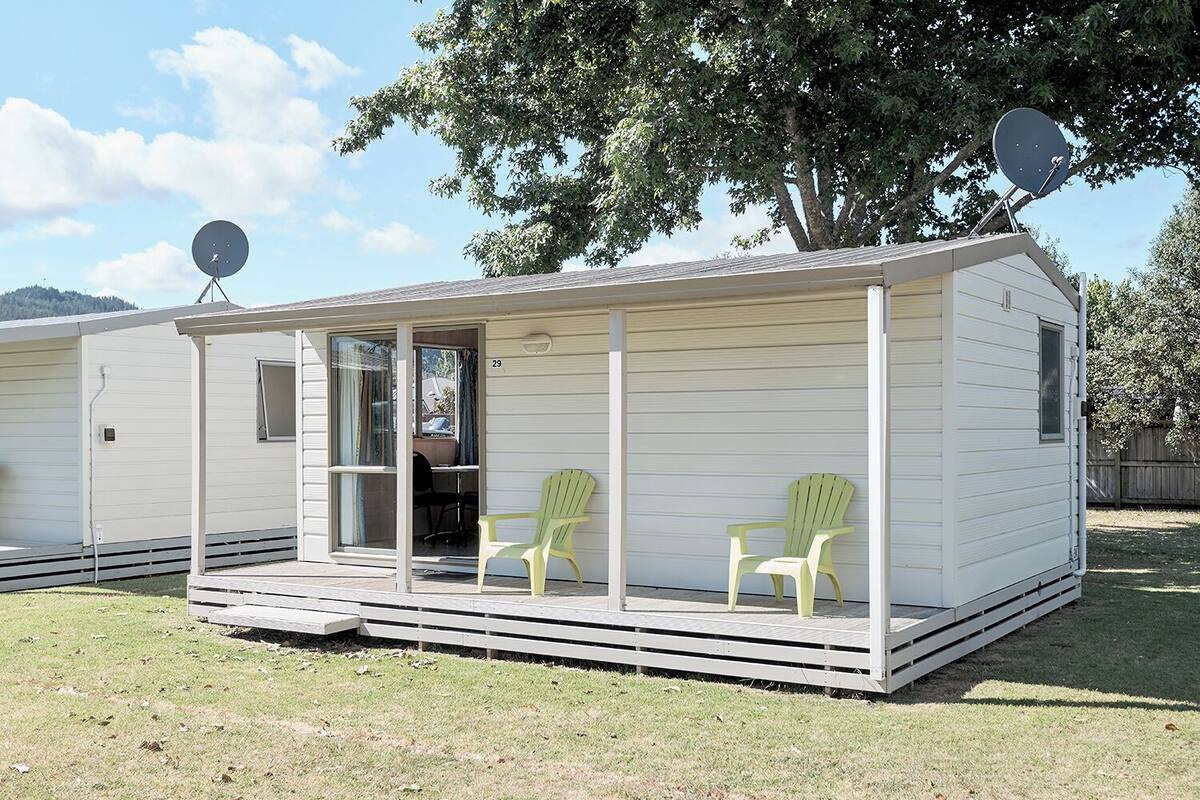 Une maison mobile dotée d’un porche couvert, de deux chaises et d’antennes paraboliques.