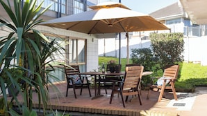 An outdoor patio with a table and chairs, a large umbrella, and potted plants. - Epsom Motel (Auckland)