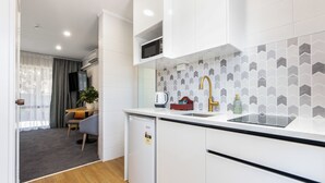 A modern kitchen with white cabinetry, a black countertop, and a herringbone tile backsplash. - Epsom Motel (Auckland)