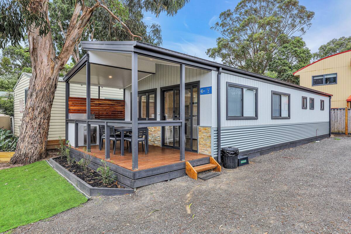 A modern mobile home with a covered porch, a small deck, and a well-maintained garden.