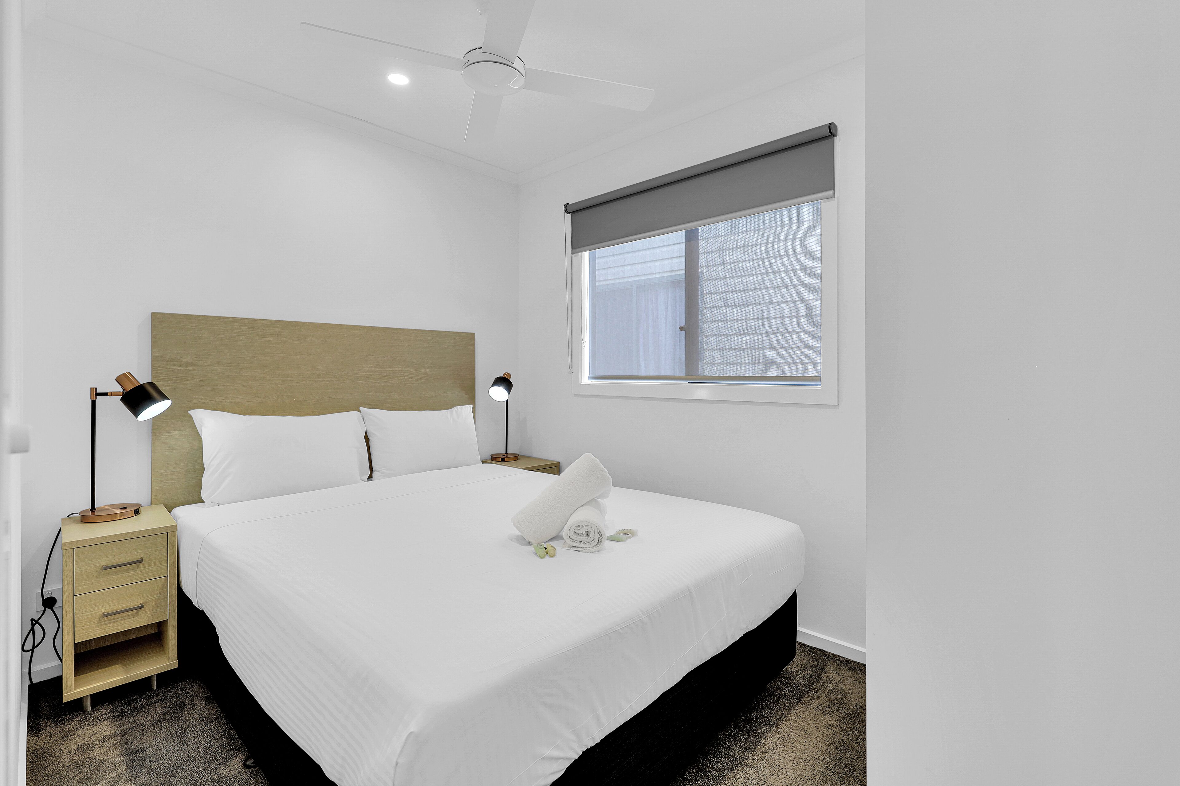 A neatly made bed with white linens, a wooden headboard, and a bedside table with a lamp.