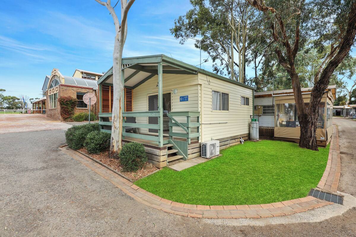 A mobile home with a covered porch, a small lawn, and a tree in the yard.