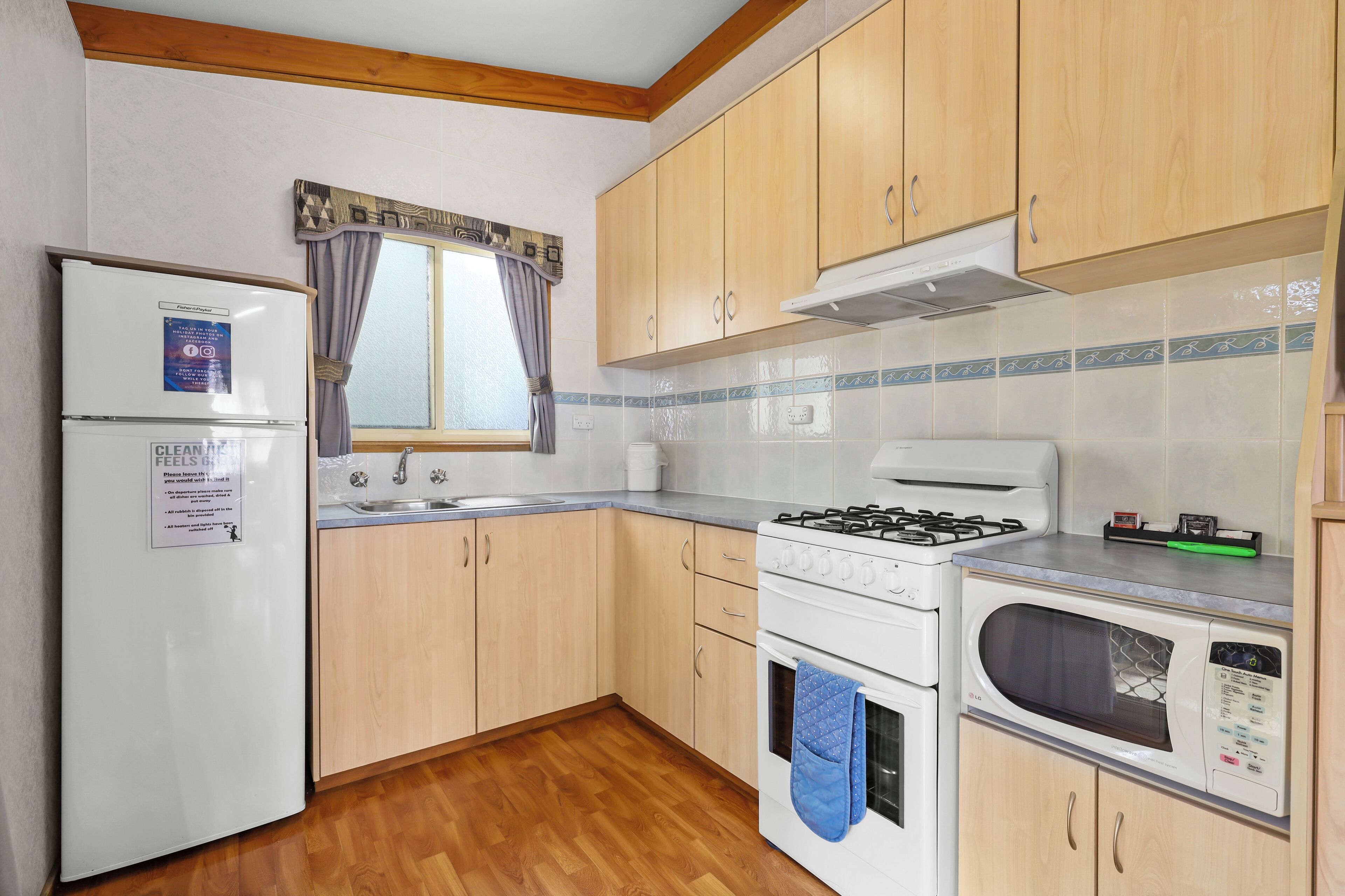 Una cocina compacta con armarios de madera, un refrigerador, una estufa, un microondas y un ventanal con cortinas.
