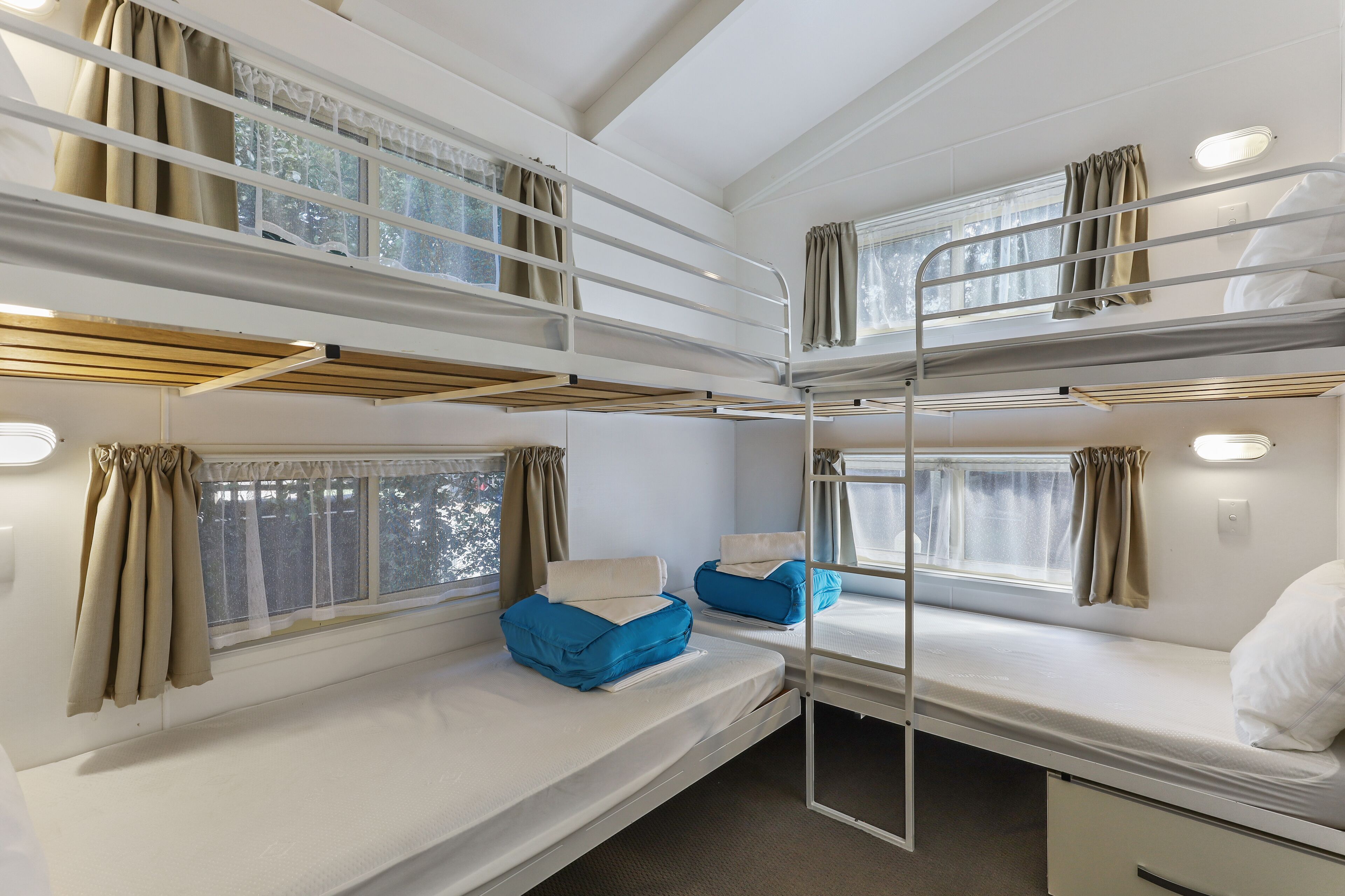 A bunk room with two beds, a window with curtains, and a bunk bed above.