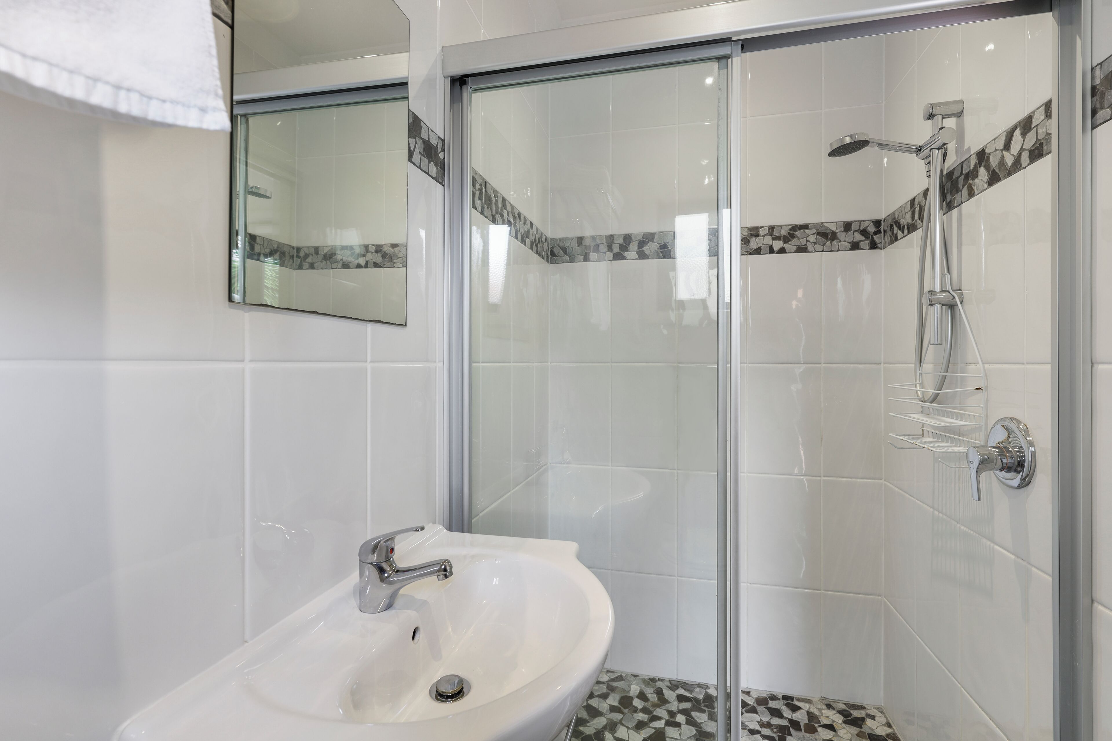 Un baño moderno con ducha acristalada, un lavamanos blanco y suelo de baldosas.