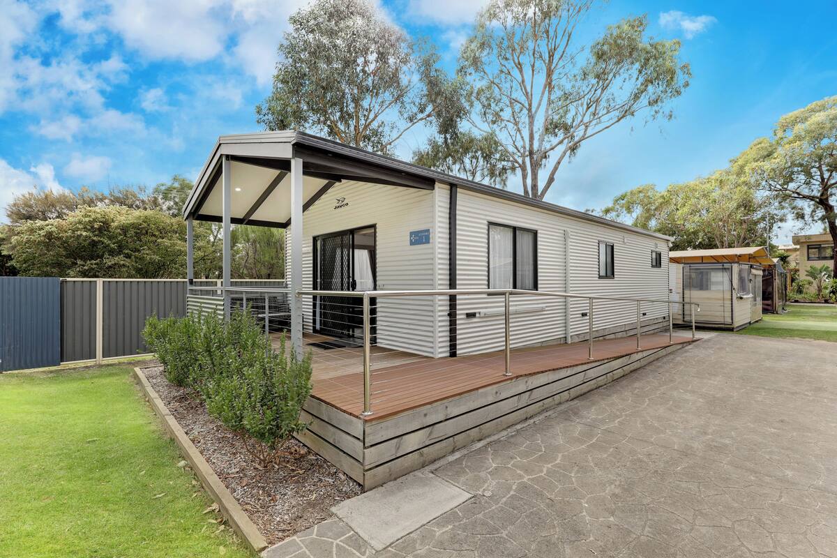 A mobile home with a covered porch, a small deck, and a paved driveway.