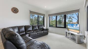 A modern living room with a leather sofa, large windows, and a flat-screen TV.