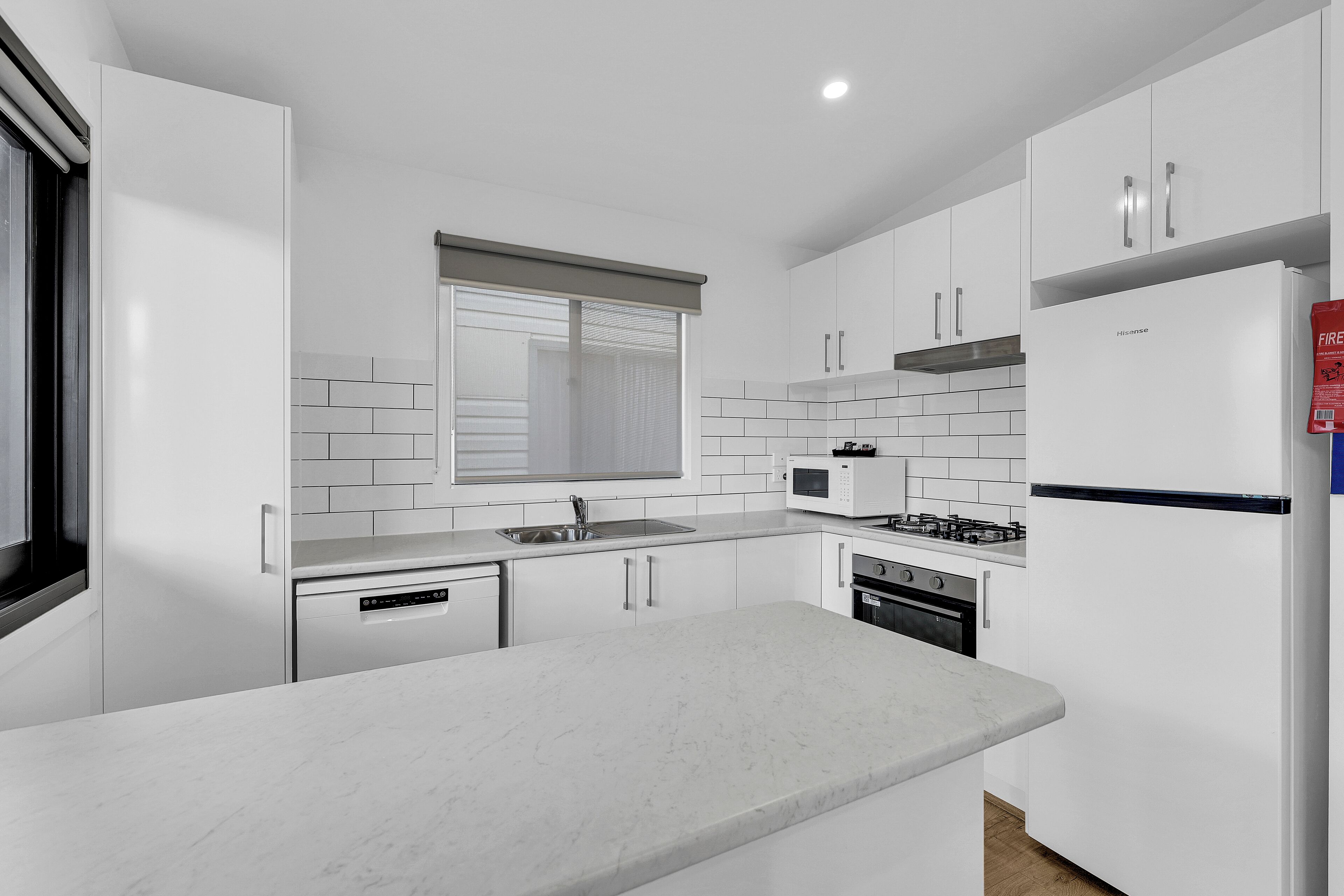 Una cocina moderna con armarios blancos, microondas integrado, estufa y lavavajillas.