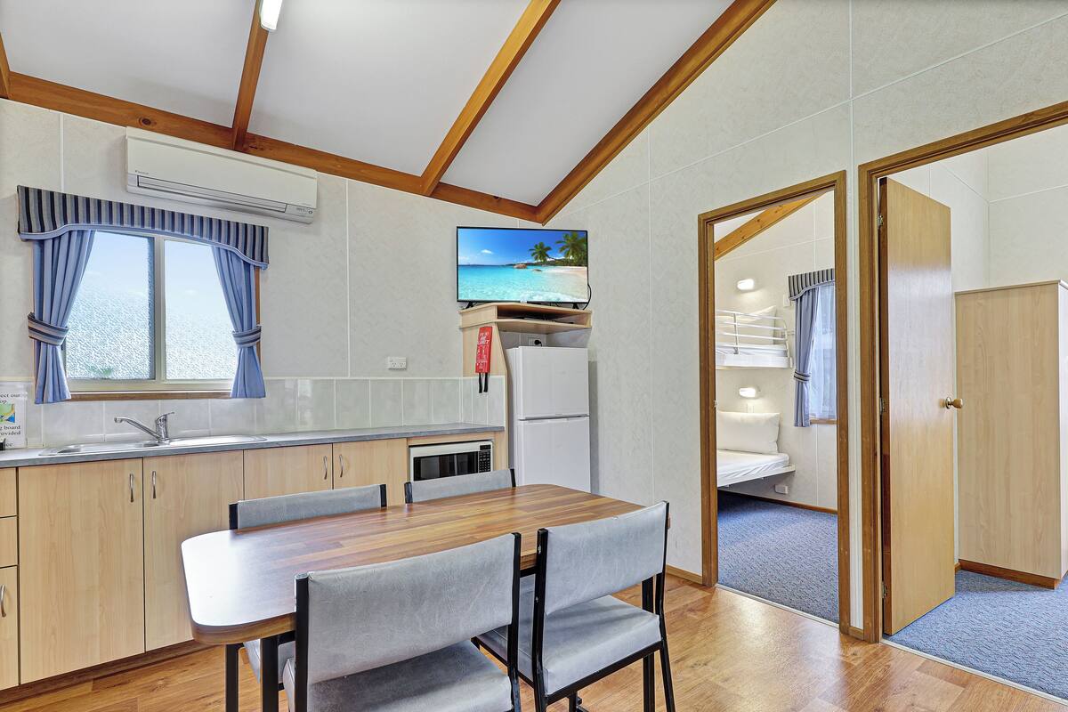 A compact kitchen with a dining area, wooden ceiling beams, a built-in air conditioner, and a view of the sea through the window.