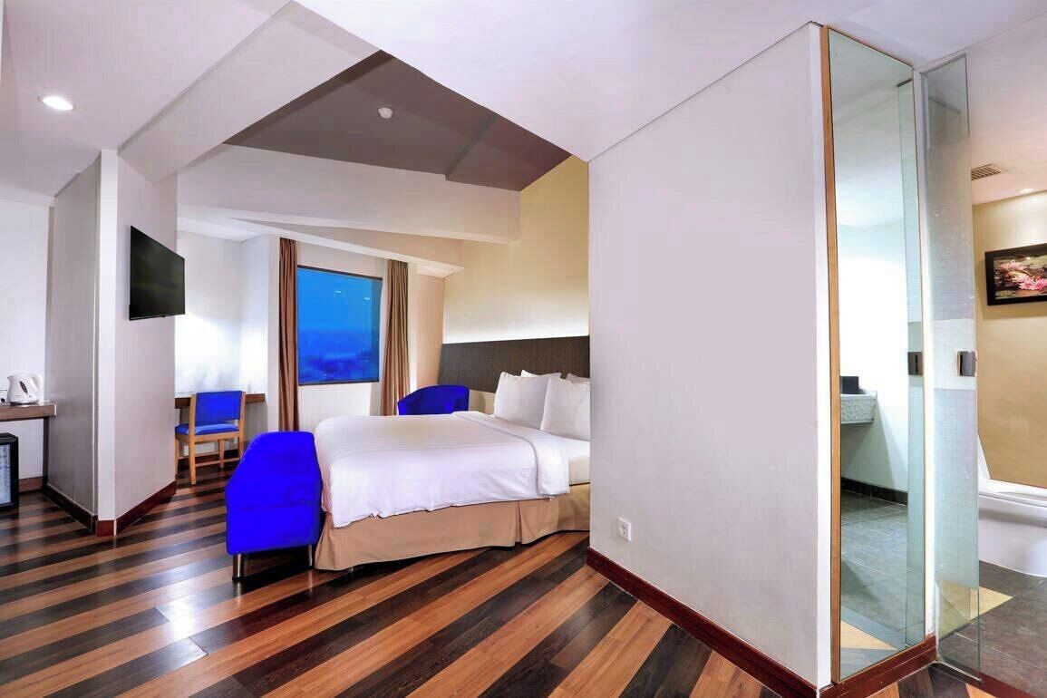 Ein Hotelzimmer mit einem Bett, einem Schreibtisch mit Stuhl, einem Fernseher und einem großen Fenster.