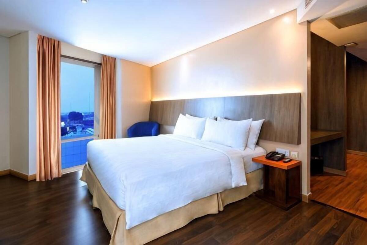 A hotel room with a large bed, a desk with a telephone, and a view through a window.