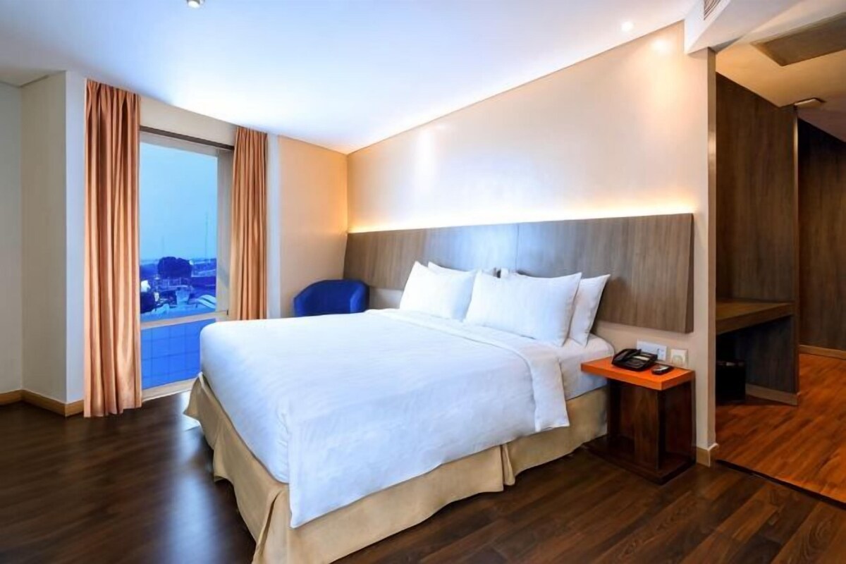 Een hotelkamer met een groot bed, een bureau met telefoon en uitzicht door een raam.